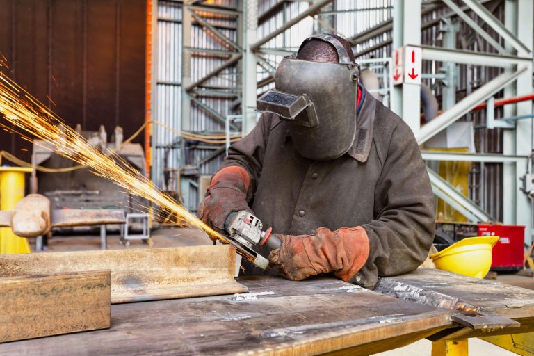 african man in the factory wearing a mask and working with a grinder, sparks flying